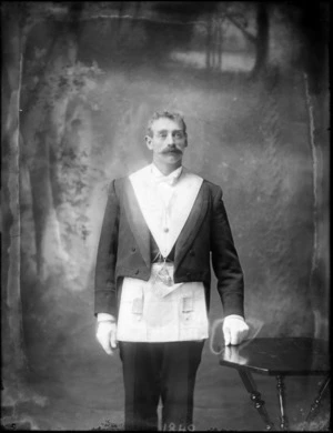 A full portrait of a unidentified man dressed in a Masonic apron and sash, standing next to a table in the studio, probably Christchurch district