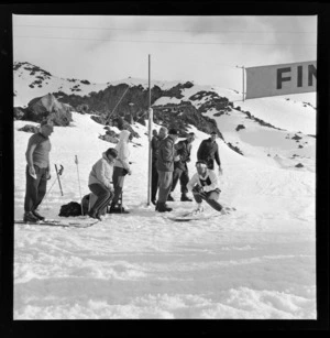 An unidentified skier touching the finish line at the New Zealand Ski Championship, Mt Ruapehu, including ski officials