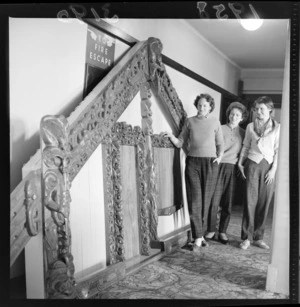 Three unidentified young women standing beside a Maori carving representing the front of a meeting house, identified as the trophy for 'Glyslalom' [?] at Chateau Tongariro