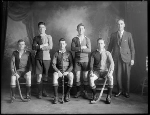 Studio portrait of unidentified men's hockey team and coach, probably Christchurch district, men seated holding hockey sticks
