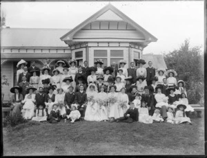 Large unidentified wedding group outdoors in front of a house, showing bride and groom, wedding party and extended families, probably Christchurch district