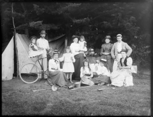 Group of unidentified men, women and girls outside a tent, possibly Sumner, Christchurch; shows one little girl sitting on bicycle