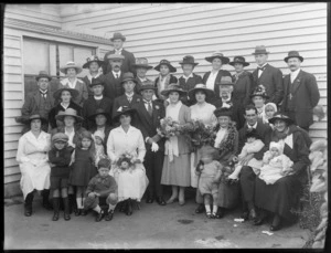 Unidentified outdoor wedding group portrait with bride and groom, priest, extended family wearing hats, children and babies, probably Christchurch region