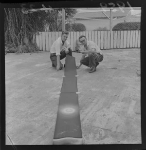 Two unidentified men with a strip of film on the concrete outside for a cartoon being produced in Levin