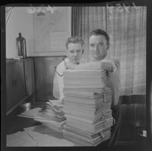Two unidentified men sitting at a desk with a stack of paper [finished cartoon?] for a cartoon film being produced in Levin
