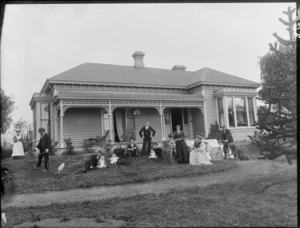 Unidentified group, probably a family, in front of wooden house with veranda, with man watering lawn, bicycles and dog, white cockatoo in a cage, maid behind, probably Christchurch region