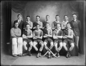 Studio portrait of unidentified men's hockey team in uniform with pads, hockey sticks and small cup in front, Christchurch