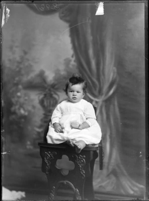 Studio portrait of an unidentified child, sitting on a carved wooden chair, possibly Christchurch