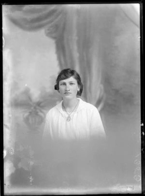 Head-and-shoulders studio portrait of an unidentified young woman, who is wearing a necklace with an inset photograph of a man