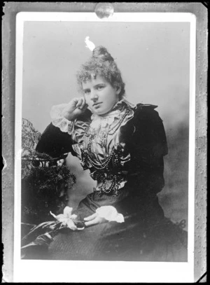 Studio portrait of unidentified woman, wearing a bodice decorated with swagged beads, holding a flower, probably Christchurch district