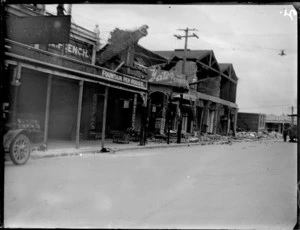 Napier earthquake damage, view of large collapsed brick buildings, with workmen pulling down upper story level using traction engine and cables, next to 'Yates Cash Store', Napier, Hawke's Bay District