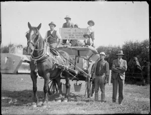 New Napier Week Carnival, horse drawn wagon with dustmen and children, holding sign 'The 4 Future Dustmen For a New Napier, We Grow To Serve', wooden tank behind, Napier, Hawke's Bay District