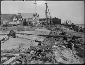 [Napier earthquake damage?] view of Port of Napier wharf area, looking to damaged road in foreground adjacent to the harbour, warehouses and ships at dockside beyond, Napier, Hawke's Bay District