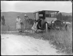 Three unidentified women with car parked by the side of the road having a cup of tea, with campfire and kettle, farmland beyond, Hawke's Bay Area.