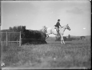 View of a woman and horse jumping a thatched fence in an unidentified competition, Hawke's Bay District