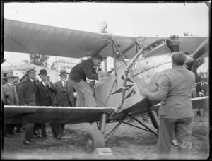 Close-up view of a man climbing into a Tiger Moth bi-plane, with spectators behind, Hawke's Bay District