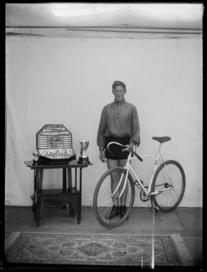 Cycling champion indoors with bike and cups, [Hastings?], Hawke's Bay District