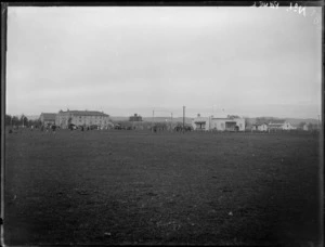 Maori Agricultural College, view of people out in front of school buildings, with water tanks and neighbouring houses, as viewed across a field, Te Hauke, Kahuranaki, Hawke's Bay District
