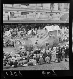 Festival of Wellington parade, showing a parade float representing the nursery rhyme 'There Was an Old Woman Who Lived In a Shoe', surrounded by spectators, outside the DIC building, Lambton Quay, Wellington