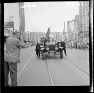 Festival of Wellington parade, showing unidentified men in firemen's uniforms pushing a fire truck, onlookers, and buildings on Dixon Street, Wellington