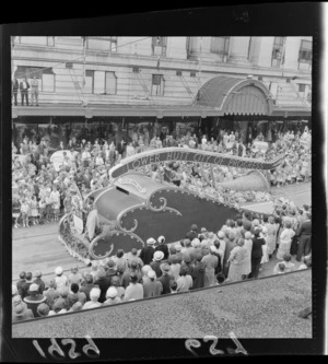 Festival of Wellington parade, showing parade float representing Lower Hutt, with two unidentified men, one in traditional Maori costume, forming a [coat of arms?] tableaux at rear of float, Lambton Quay, Wellington