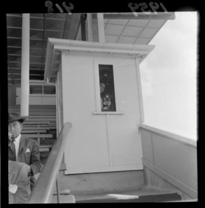Unidentified man holding a camera, in a booth at Trentham Racecourse, Upper Hutt