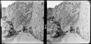 Horse and cart travelling along a road with steep rocky slopes on either side [Central Otago?]