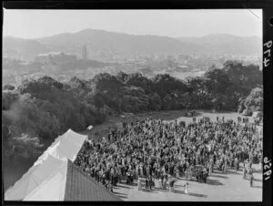 View of marquee and crowd at garden party on front lawn of Government House, Wellington, taken from the house and with city, including National Museum on Buckle Street, in background