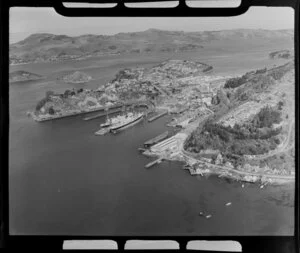 View of Port Chalmers, Dunedin City, showing Carey's Bay in foreground with boat sheds, then port area with wharfs and ships, commercial and residential buildings, looking to Portobello across inner harbour