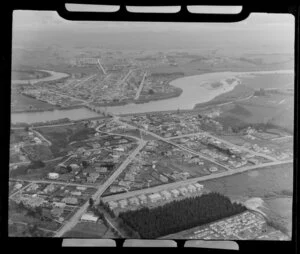 Balclutha, Otago District, showing Milton Highway (State Highway 1) through residential housing next to pine plantation hiding local cemetery, bridge over Clutha River to township with sports grounds, farmland beyond