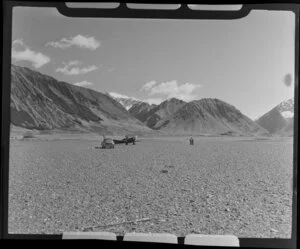 Lake Ohau, Central Otago, view of shingle river bed with a plane, a car and two men, snow capped mountains beyond