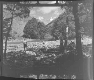 Lake Ohau, Central Otago, view of upper Temple Valley with rock covered riverbed, with man walking over to river with fishing rod, looking up tree covered valley with snow covered mountains beyond