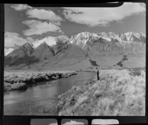 Lake Ohau, Central Otago, view of upper Huxley Valley with tussock covered valley and stream with fisherman and rod, snow covered mountains beyond