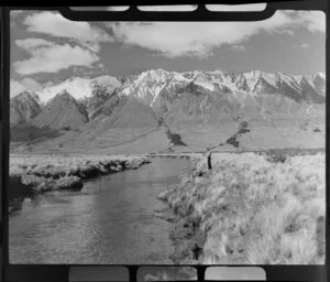 Lake Ohau, Central Otago, view of upper Huxley Valley with tussock covered valley and stream with fisherman and rod, snow covered mountains beyond