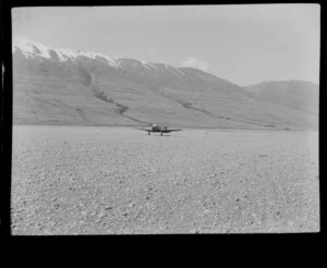 Lake Ohau, Central Otago, view of shingle river bed with Mount Cook Whitley Straight (ZK AUK) tourist aircraft taking off, snow covered mountain range beyond