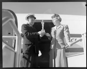 Unidentified man and woman holding an Oscar statuette next to Pan American World Airways aircraft, Whenuapai Airport, Auckland
