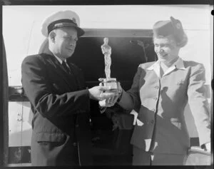 Unidentified man and woman holding an Oscar statuette next to Pan American World Airways aircraft, Whenuapai Airport, Auckland