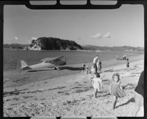 Auster aircraft ZK-AYO at Paihia; children and adults on beach