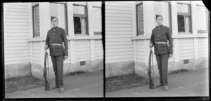 Edgar Richard Williams in military uniform standing outside house and holding a rifle, Dunedin, Otago Region