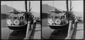 [Edgar Richard or Owen William Williams] standing on wharf beside ferry with the Remarkables in background, Lake Wakatipu, Queenstown-Lakes District, Otago Region