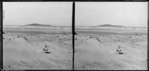 Young child, seated on the beach, next to a hat, [Taieri Island?], South Otago