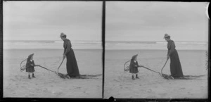 Unidentified woman and child, playing with seaweed on the beach, Taieri area, South Otago