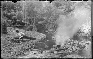 Owen or Edgar Williams lounging on a stony bank beside a stream, unknown location