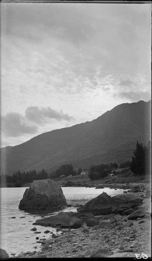 Large rocks on the shore of Lake Wakatipu, Queenstown, including houses in distance and clouds overhead