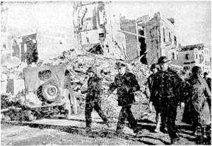 Against a background of buildings shattered by the guns of the Allied warships during their bombardment of the town, Admiral Sir John Cunningham picks his way through quayside debris at Anzio, on the coast south of Rome. He is accompanied by Allied officers. (Evening Post, 11 March 1944)