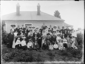 Unidentified large wedding group, showing bride and groom, wedding party and family members outside a wooden house, probably Christchurch district