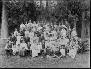 Large group of men, women and children, sitting outside beneath trees, probably Christchurch district