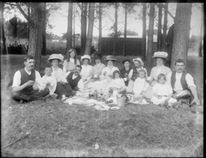 Unidentified group of men, women and children at a picnic, probably Christchurch district, shows them sitting around food and drink
