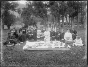 Unidentified group picnicking, showing men, women and children sitting around food laid out on a cloth, probably Christchurch district