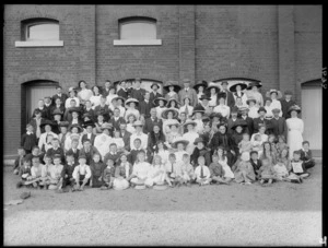 Unidentified large group of men, women, and children, with brick building behind, probably Christchurch district